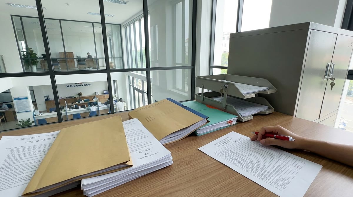 Phòng vận hành ngân hàng Việt Nam với hồ sơ giấy, bút đỏ và khay lưu trữ an toàn